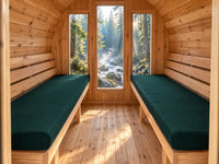 Forest green cushions on two benches inside a barrel sauna overlooking a woodland creek