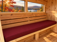 Burgundy cushion on a barrel sauna bench with autumn trees beyond the window