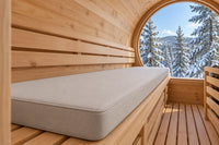 Pearl gray cushion on a barrel sauna bench beside a snowy woodland view