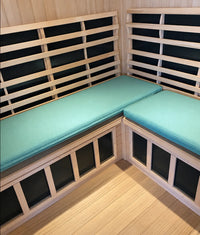 Two green sauna cushions on a wooden corner bench